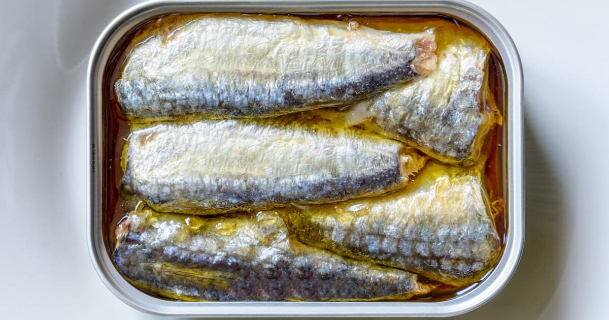 Une boîte ouverte de sardines à l'huile sur une assiette blanche vue de dessus.