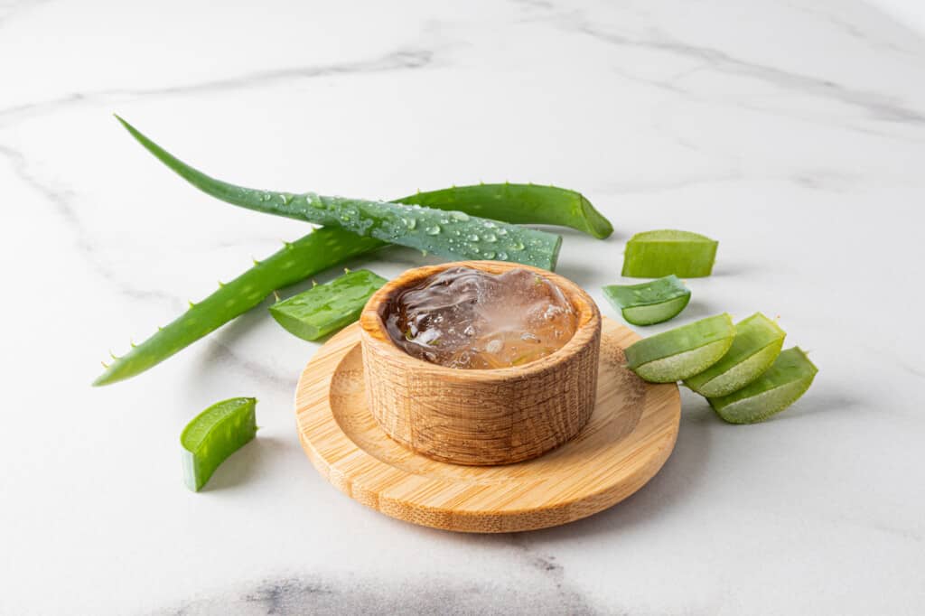 Gel d'aloe vera dans un bol en bois sur fond de marbre avec des feuilles et des tranches d'aloès frais