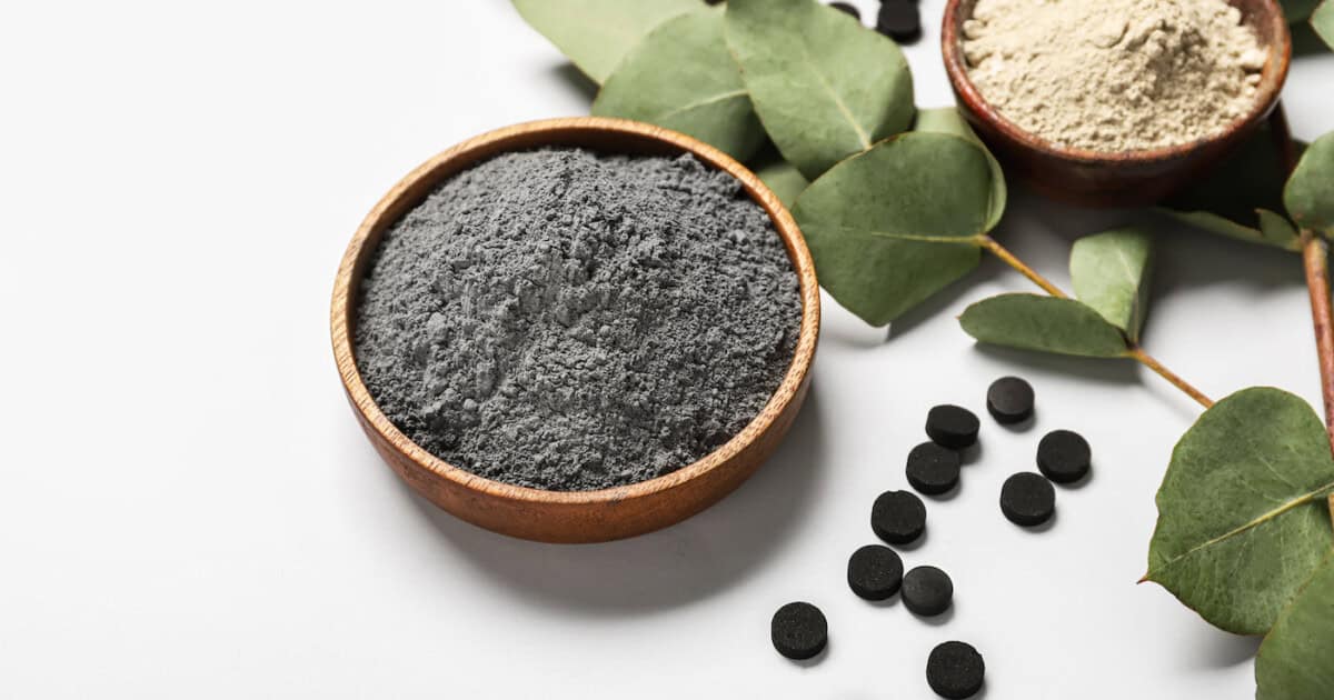 Bol de masque facial au charbon actif, pilules et branche d'eucalyptus sur fond blanc, gros plan