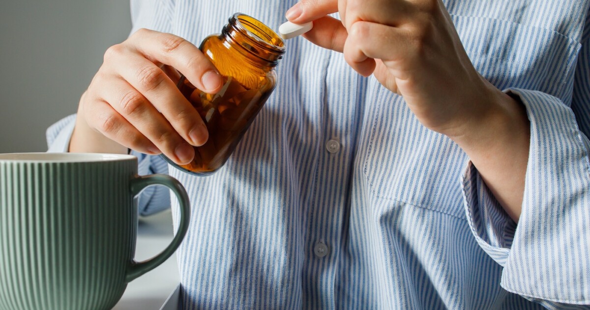 Femme prenant des pilules dans une petite bouteille en verre marron et de l'eau potable en gros plan.