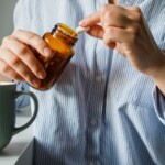Femme prenant des pilules dans une petite bouteille en verre marron et de l'eau potable en gros plan.