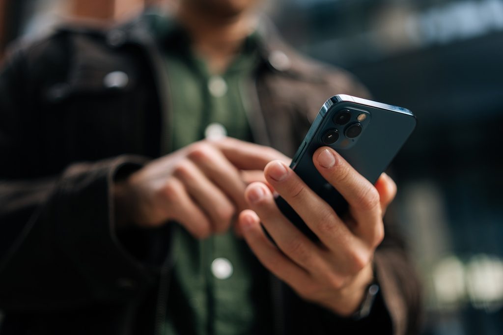 Gros plan des mains d'un homme méconnaissable tenant et utilisant un smartphone debout dans la rue de la ville.