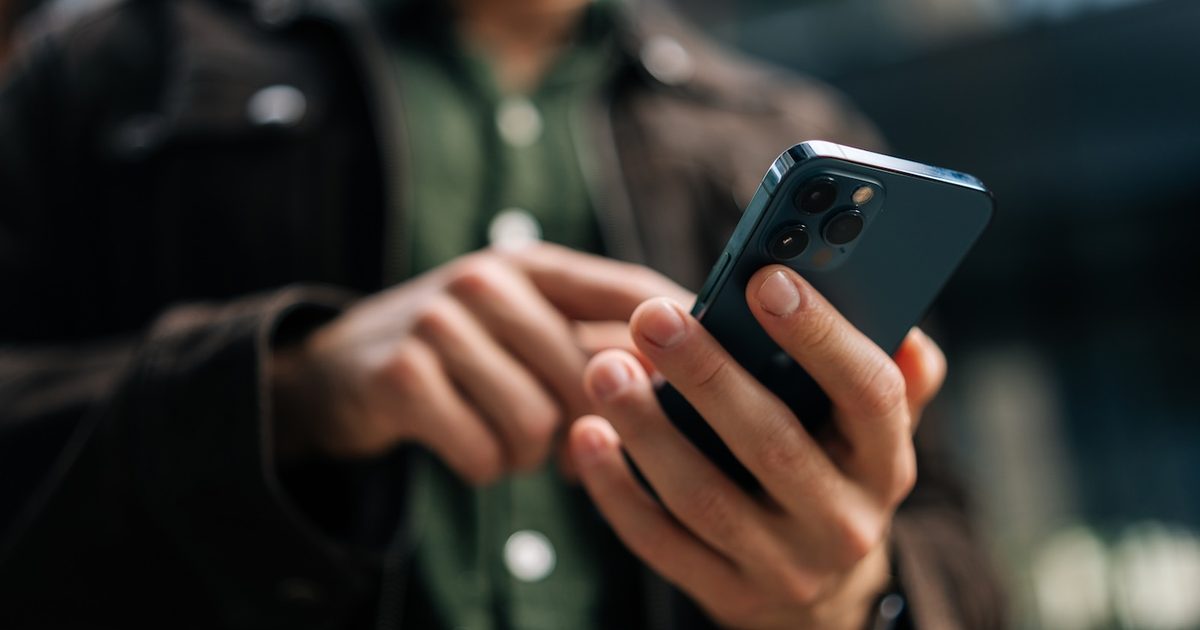 Gros plan des mains d'un homme méconnaissable tenant et utilisant un smartphone debout dans la rue de la ville.