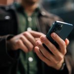 Gros plan des mains d'un homme méconnaissable tenant et utilisant un smartphone debout dans la rue de la ville.