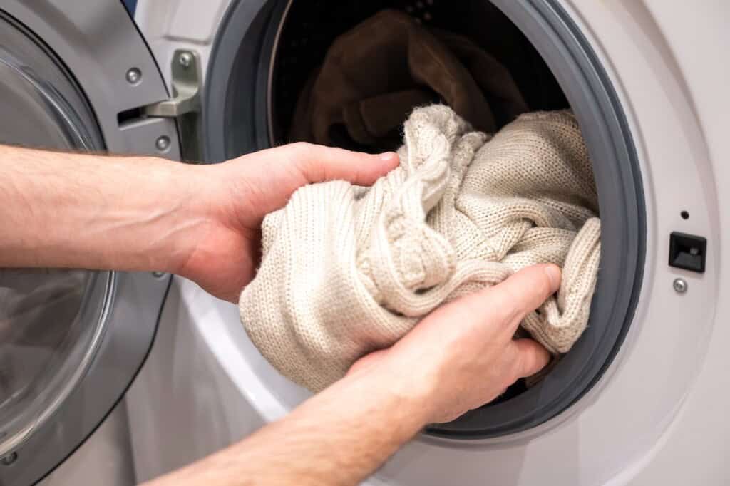 Un homme met un pull en laine beige dans la machine à laver