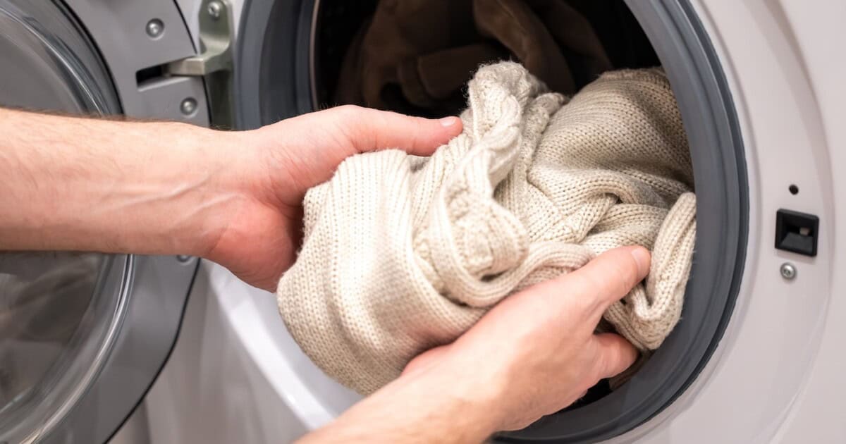Un homme met un pull en laine beige dans la machine à laver