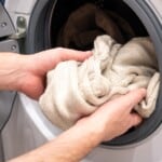 Un homme met un pull en laine beige dans la machine à laver