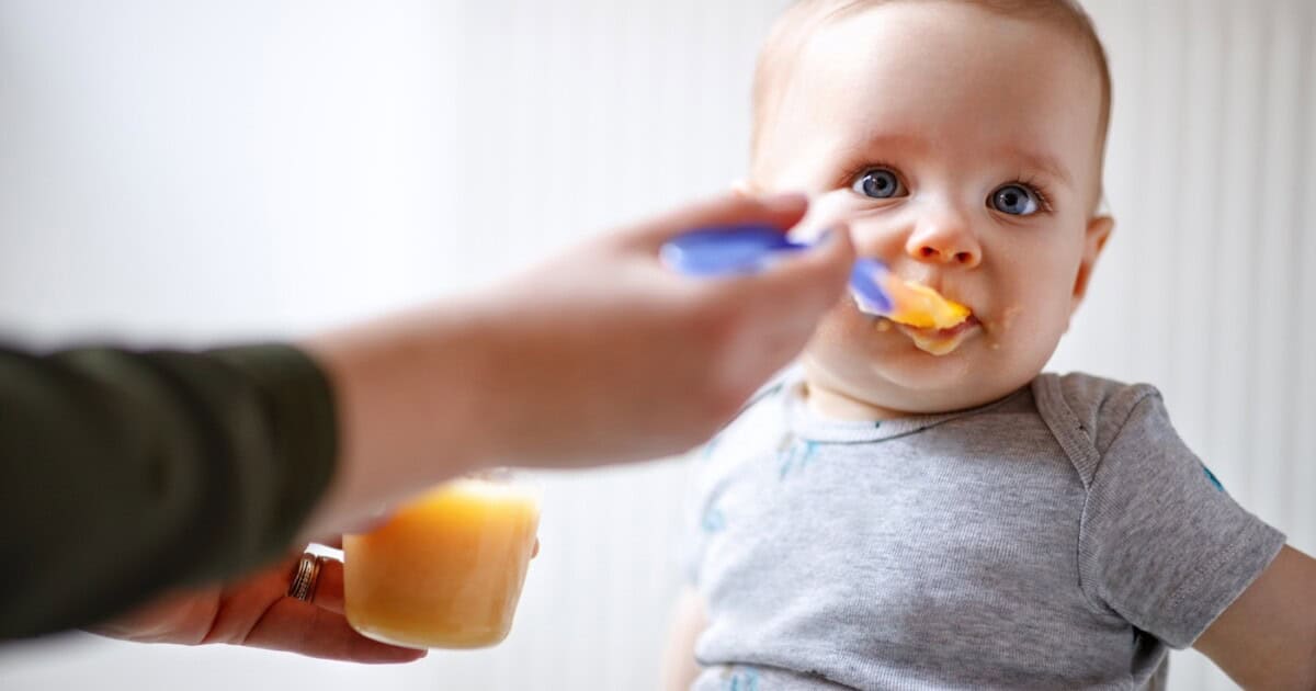 La mère nourrit un joli bébé mâle avec de la bouillie de fruits