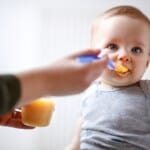 La mère nourrit un joli bébé mâle avec de la bouillie de fruits