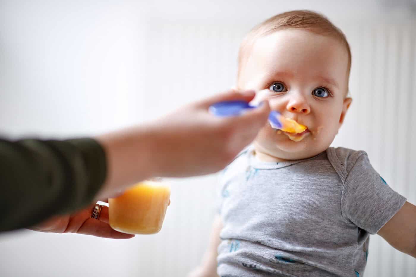 La mère nourrit un joli bébé mâle avec de la bouillie de fruits