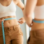 Le reflet dans un miroir d'une femme mince mesure sa taille avec un ruban à mesurer.