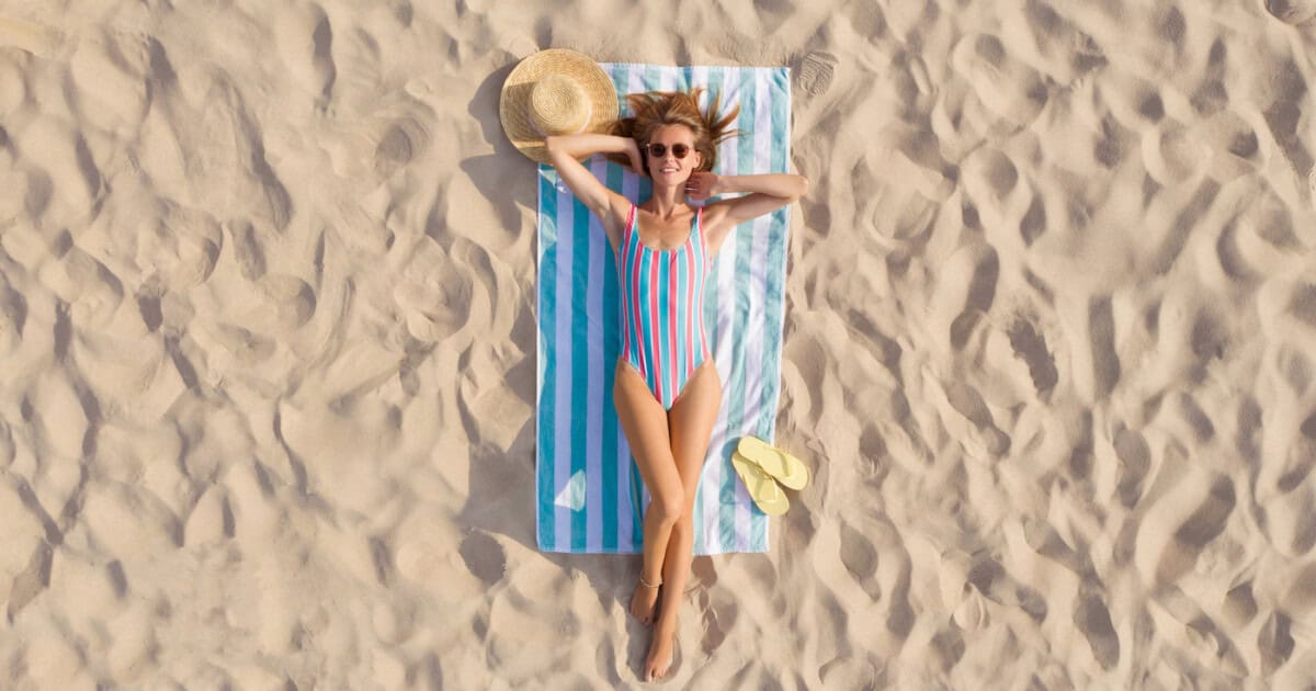 Femme en train de bronzer sur une serviette de plage sur la côte sablonneuse, vue aérienne