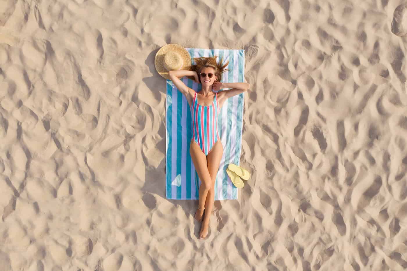Femme en train de bronzer sur une serviette de plage sur la côte sablonneuse, vue aérienne