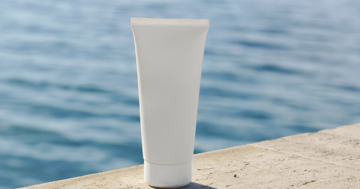 Tube cosmétique placé sur des rochers avec la mer en arrière-plan.