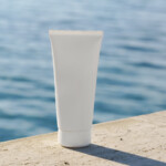 Tube cosmétique placé sur des rochers avec la mer en arrière-plan.
