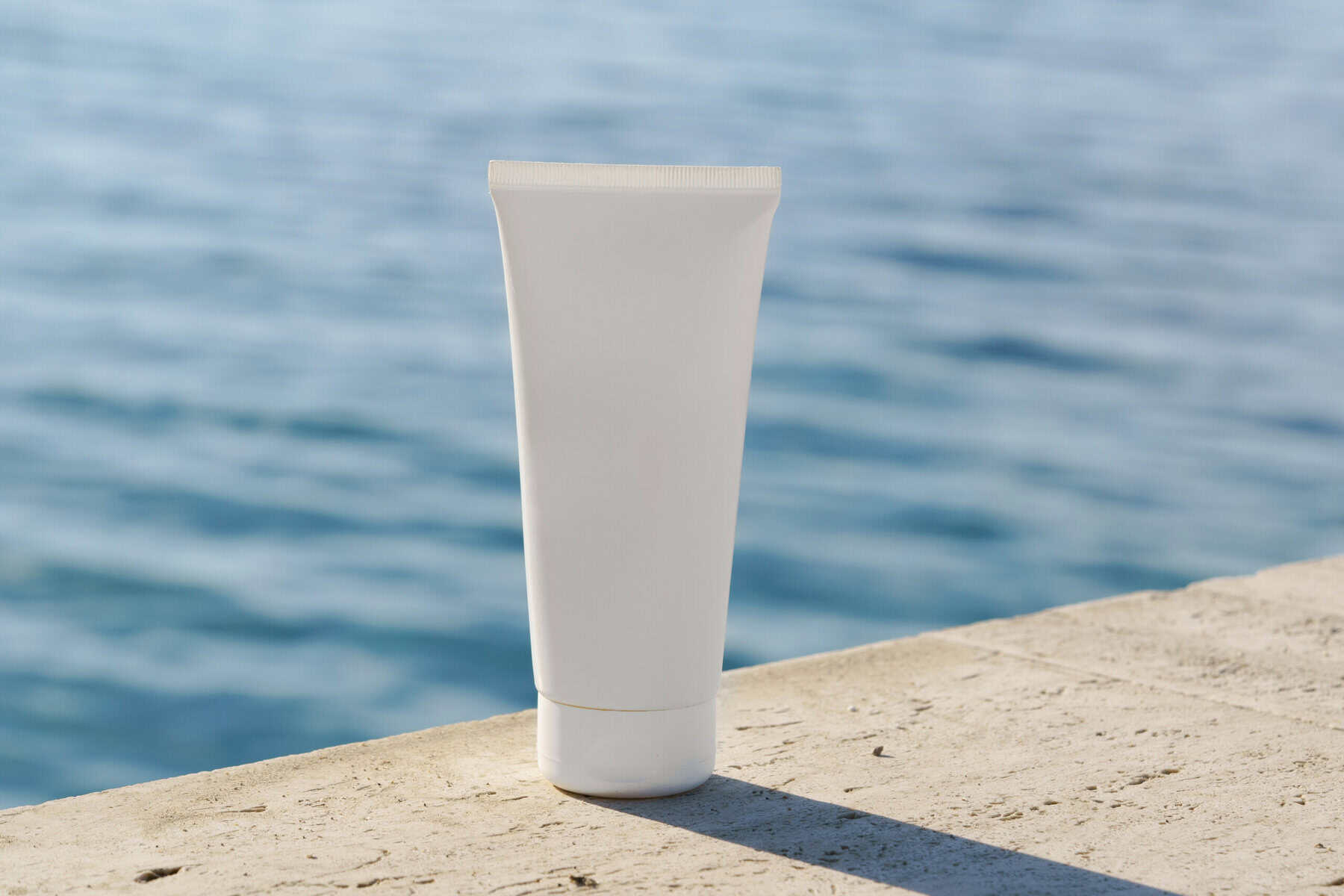 Tube cosmétique placé sur des rochers avec la mer en arrière-plan.