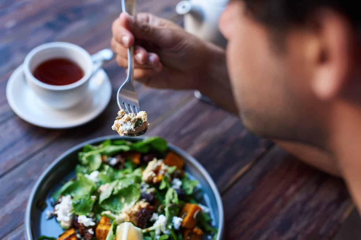 Homme mangeant une salade assis à une table de bistro