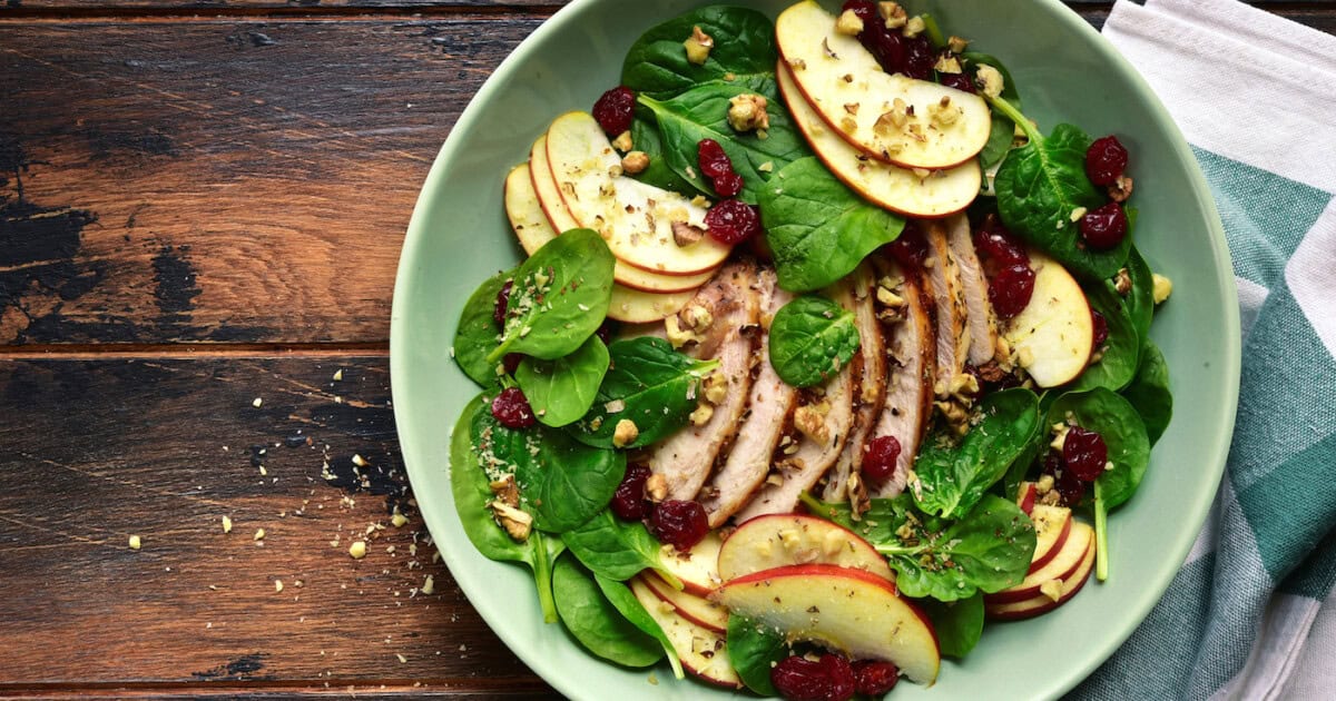 Salade fraîche avec pousses d'épinards, pomme, poulet grillé et canneberges séchées.