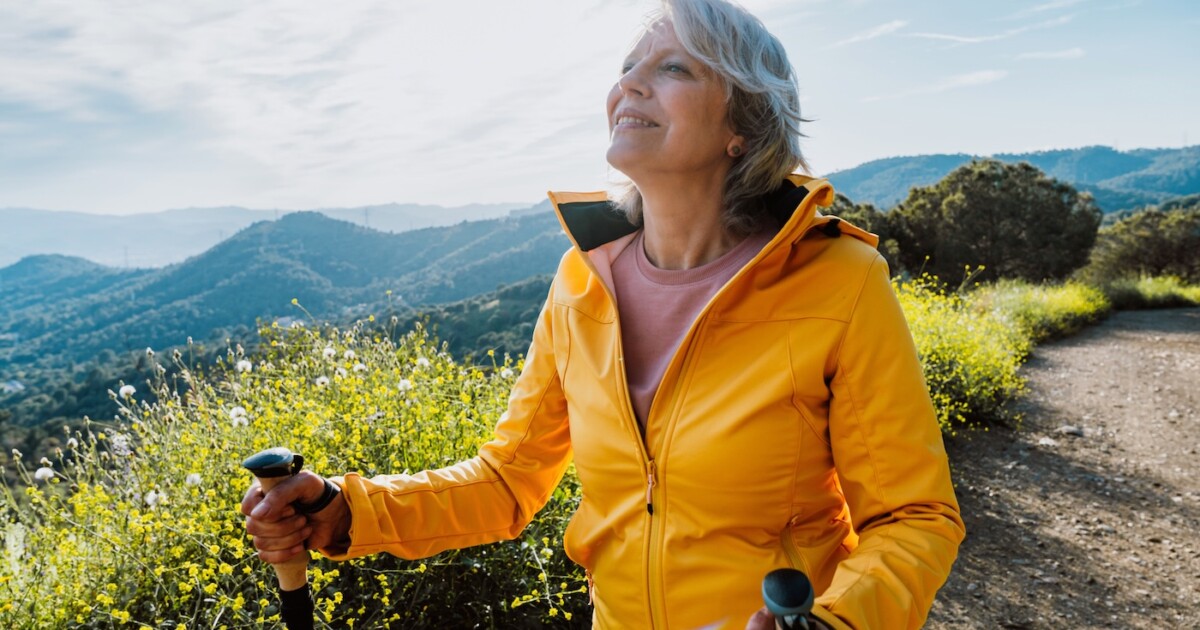 Femme âgée active faisant de la randonnée sur un sentier extérieur à l'aide de bâtons de randonnée